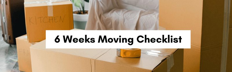 A stack of moving boxes labeled "KITCHEN" with packing tape, set in a room with a chair and plants.