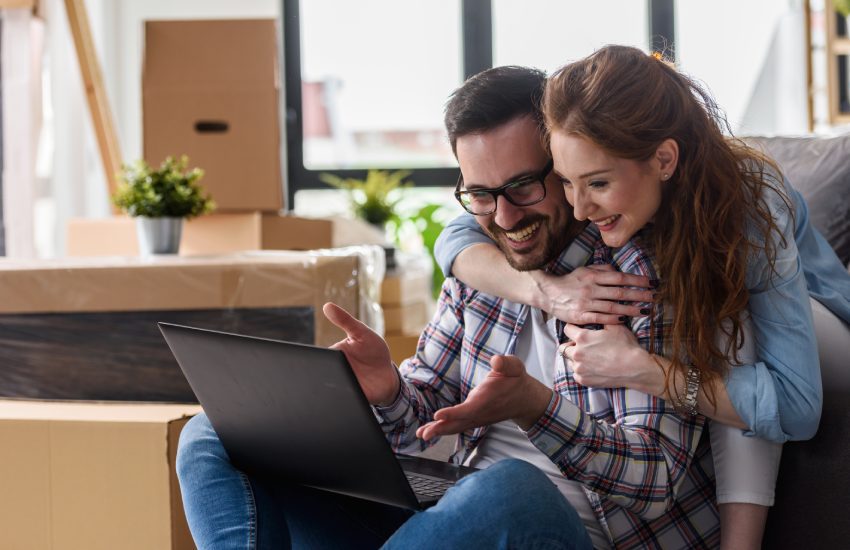 Young couple moving in new home. Sitting and relaxing after unpacking. Searching home decorating ideas on laptop