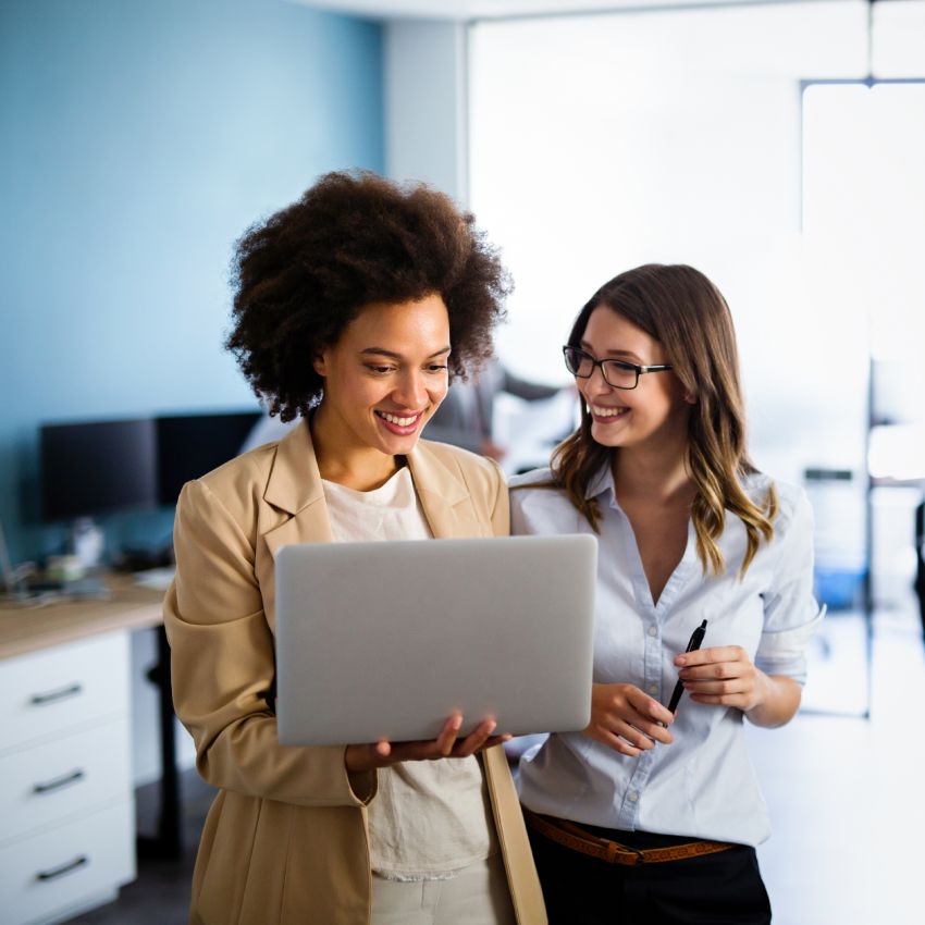 Happy multiethnic business women working together online on a laptop in corporate office.