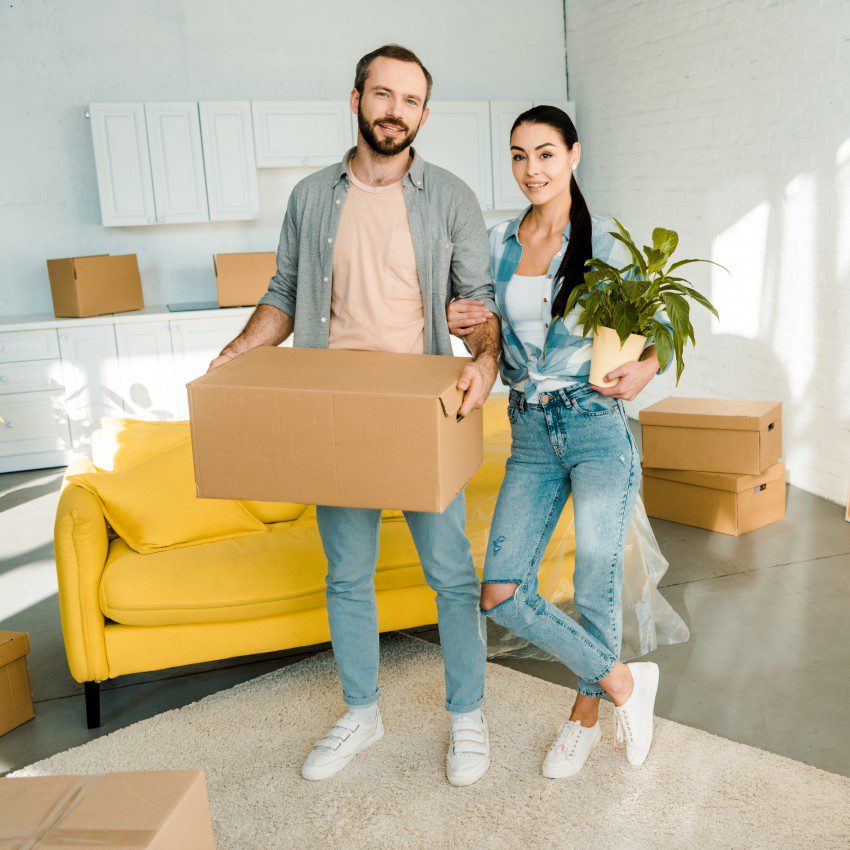 husband carrying cardboard box and wife holding green plant while packing for into new house, moving concept