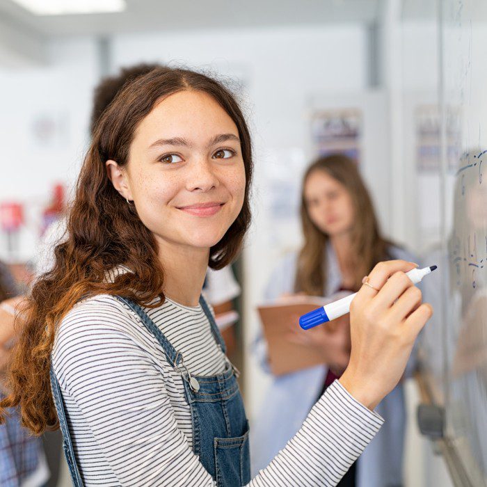 Smiling girl solving math equation on white board