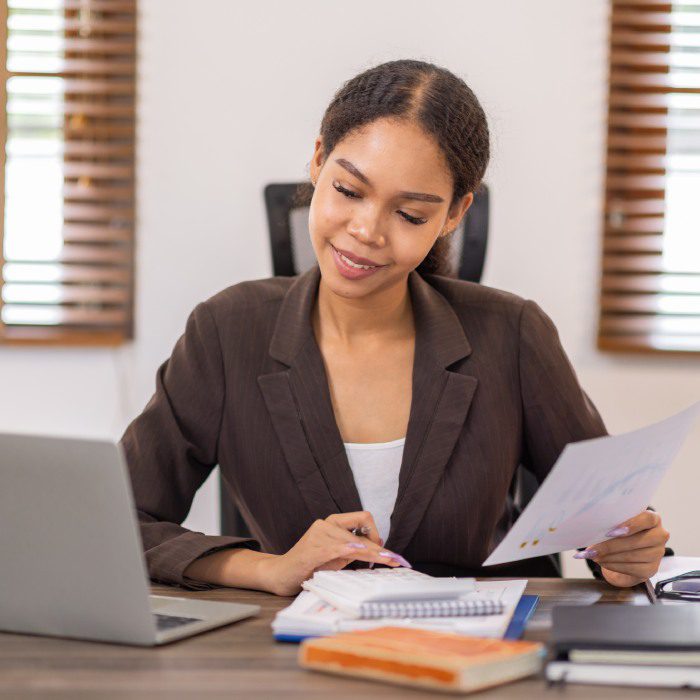 Portrait of smiling Asian Business woman using calculator and laptop for doing math finance on an office desk, tax, report, accounting, statistics, and analytical research concept