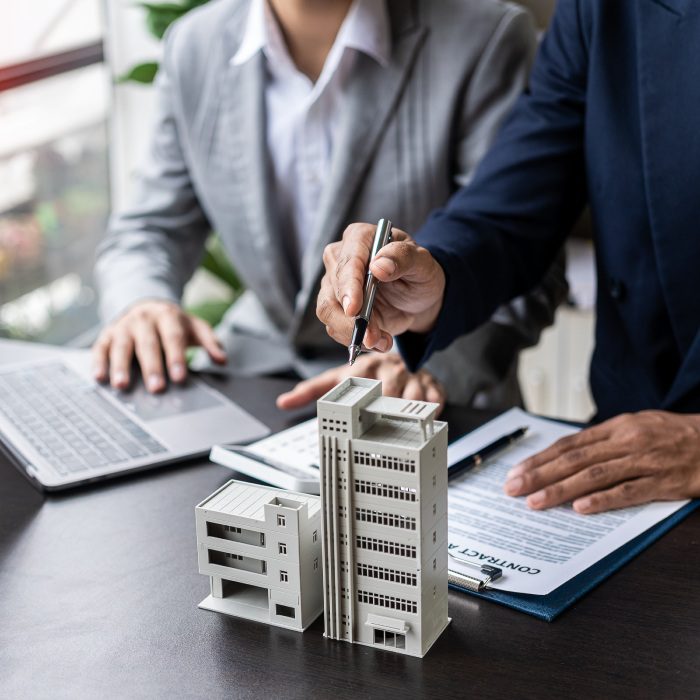 Real estate agents offer contracts to buy or rent housing. Businessman holding model small building house with property insurance at table in home sales office