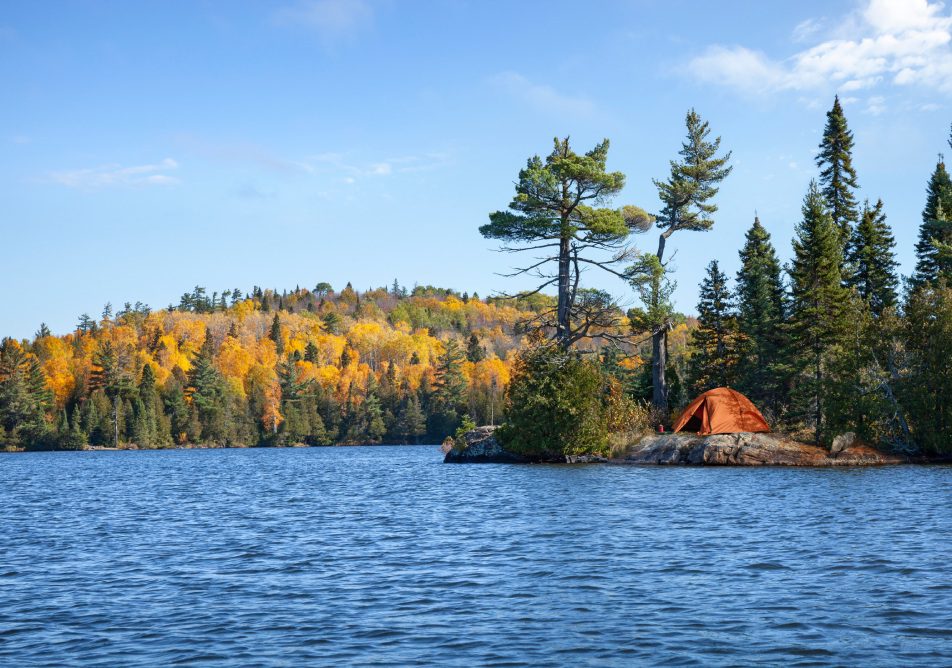 Orange tent on rocky shore of an island on a northern Minnesota trout lake during autumn