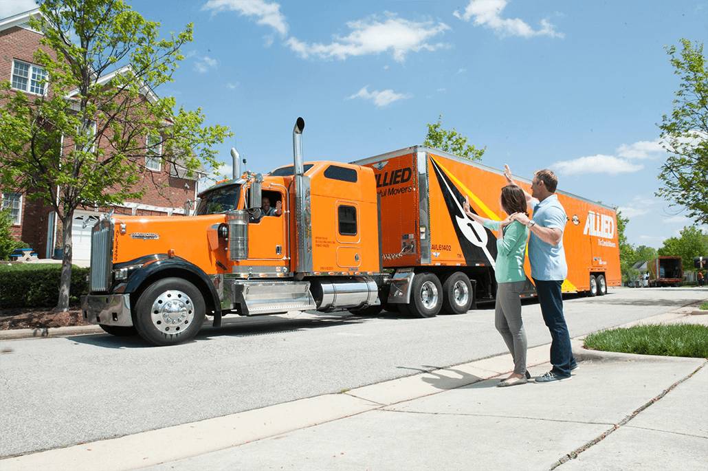 Two movers, a man and a woman, waving goodbye in front of a large moving truck