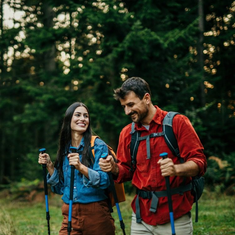 An adventurous and diverse couple eagerly explores a picturesque trail, their backpacks slung over their shoulders, and hiking sticks in hand