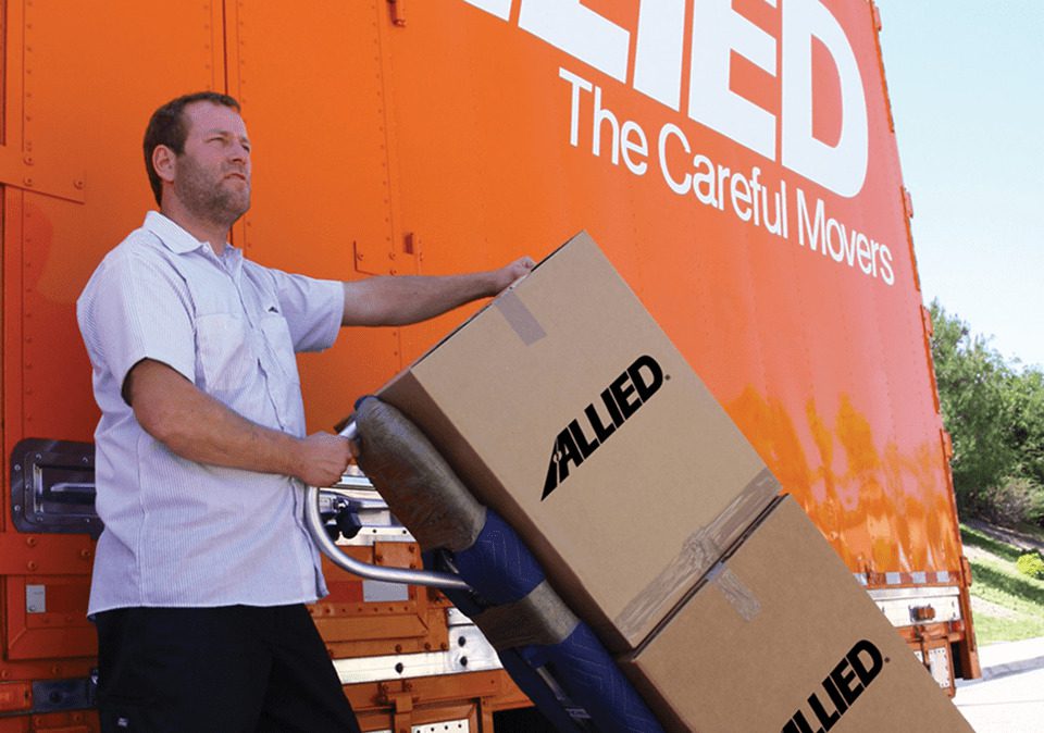 A professional Atlas Allied mover stands on a truck, holding a box, demonstrating his role in the moving process.