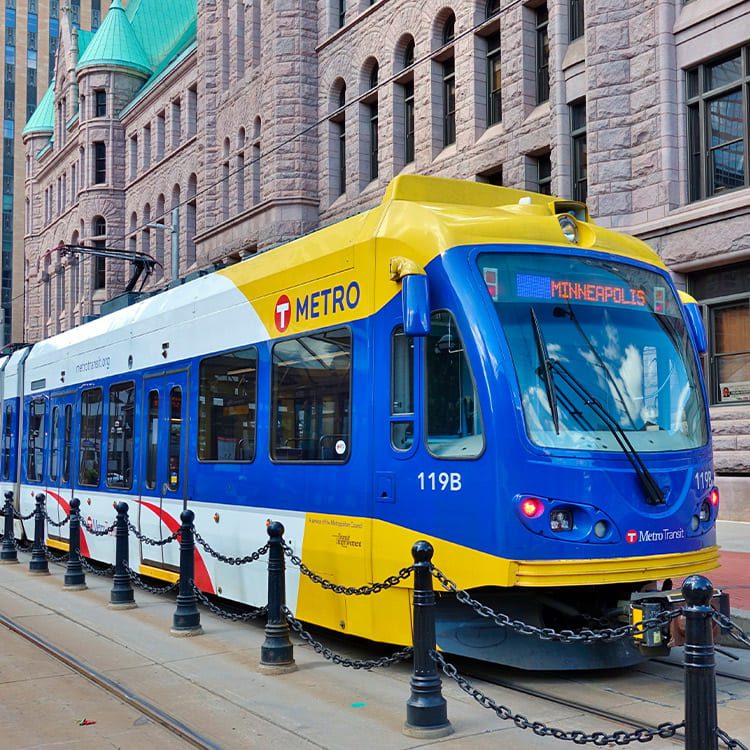 A blue and yellow train on tracks beside a building, illustrating transit options from St. Cloud to Minneapolis.