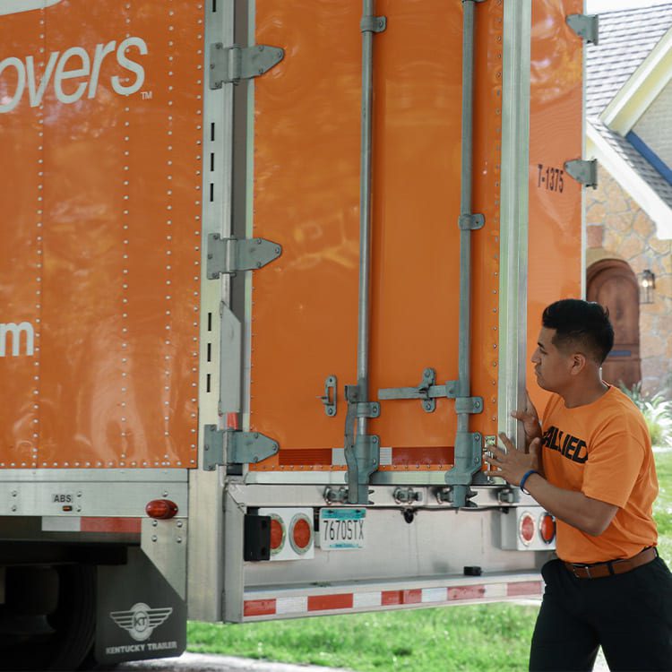 A man is loading items into a truck with a trailer attached, preparing for transport.