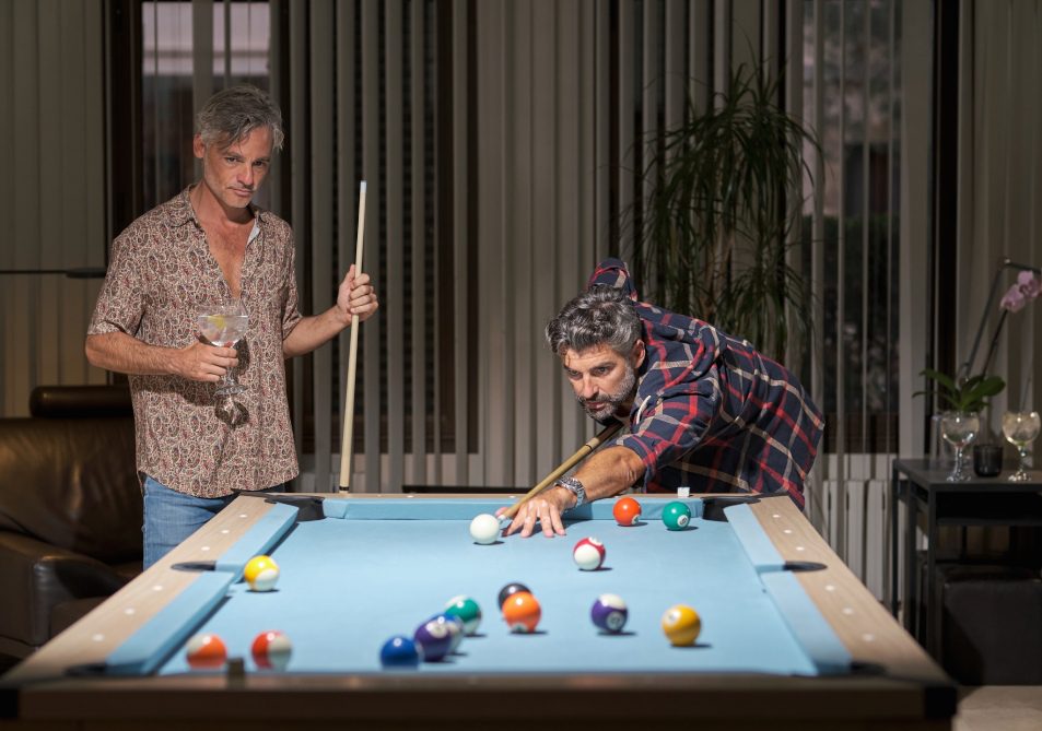Two men playing pool in a spacious room, focused on their game at the green felt table. Pool Table Movers Minneapolis