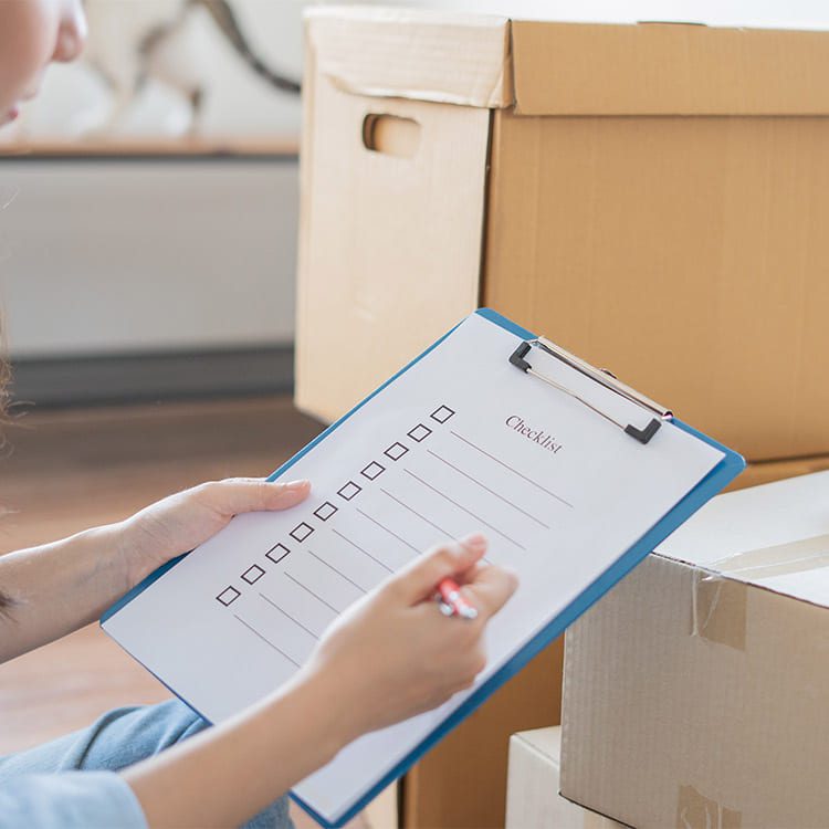A woman writes on a clipboard in front of moving boxes, illustrating steps for relocating from St. Paul to Denver.