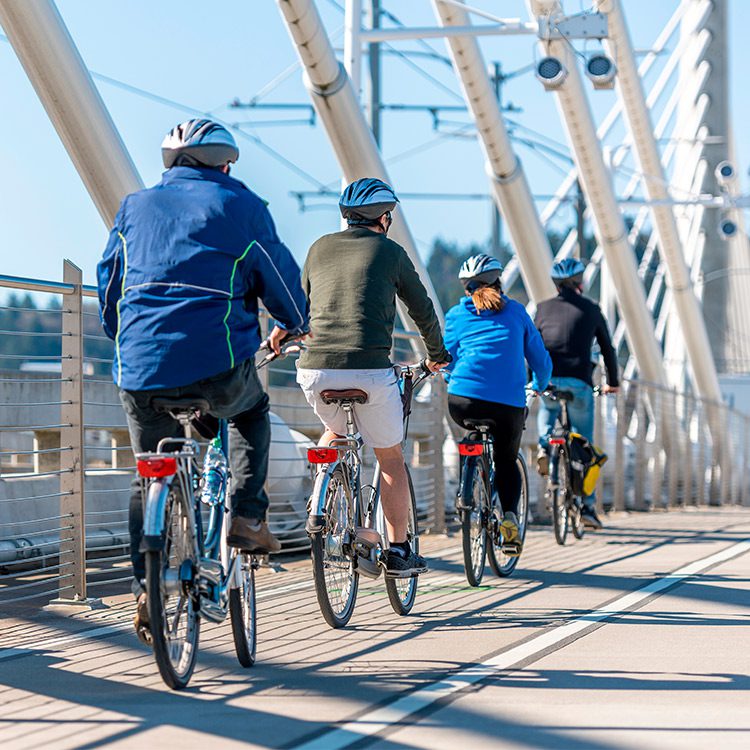 A diverse group of individuals riding bicycles on a bridge, symbolizing a journey from Minneapolis to Portland.