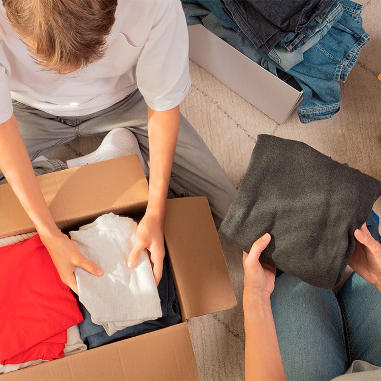 A woman and a boy pack clothes into a box, preparing for a move, as part of a guide for moving with teenagers