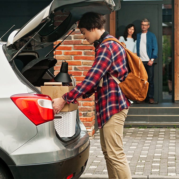 A young man loads a box into a car trunk, illustrating the moving process for families with teenager