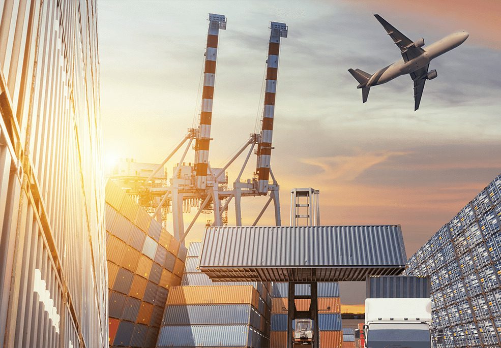 Cargo containers stacked at a shipping yard with a crane and an airplane flying overhead during sunset.