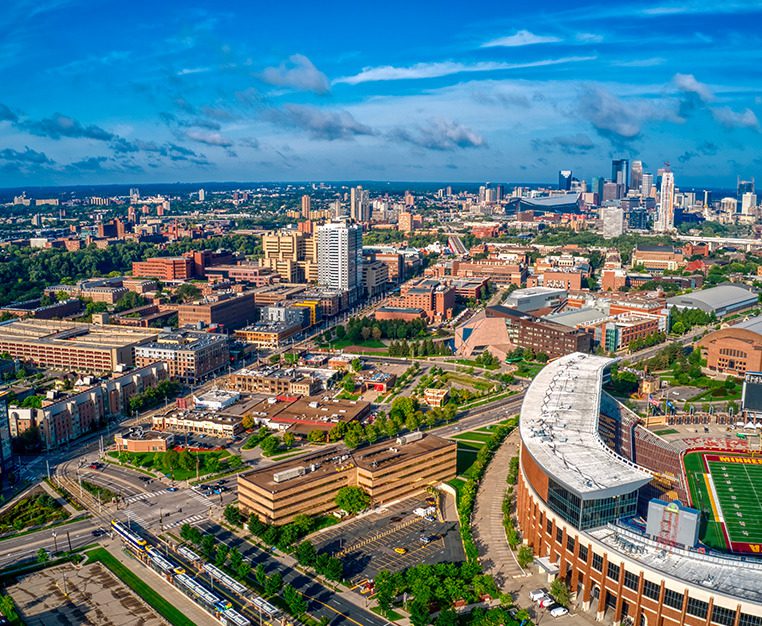 Aerial view of a vibrant urban landscape featuring buildings, parks, and a stadium, with a skyline in the background.