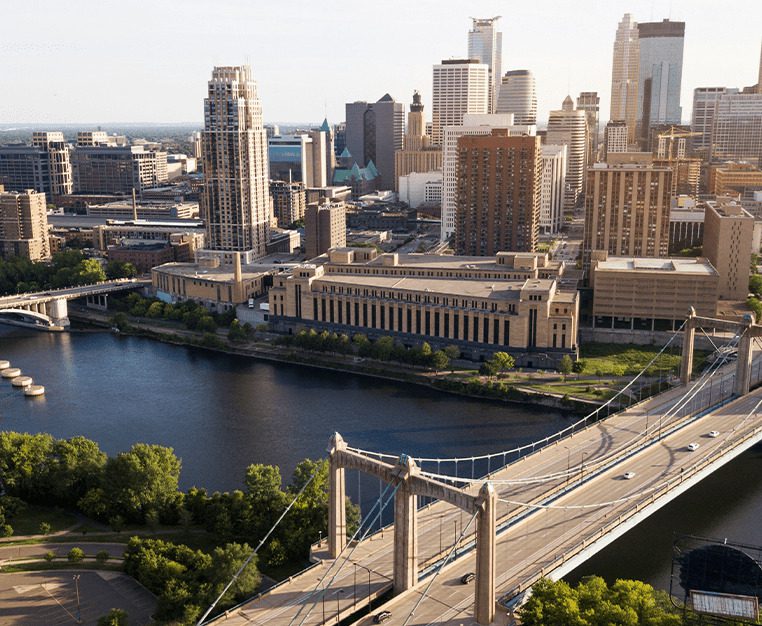 Aerial view of a city skyline featuring tall buildings, a river, and a bridge with vehicles crossing.