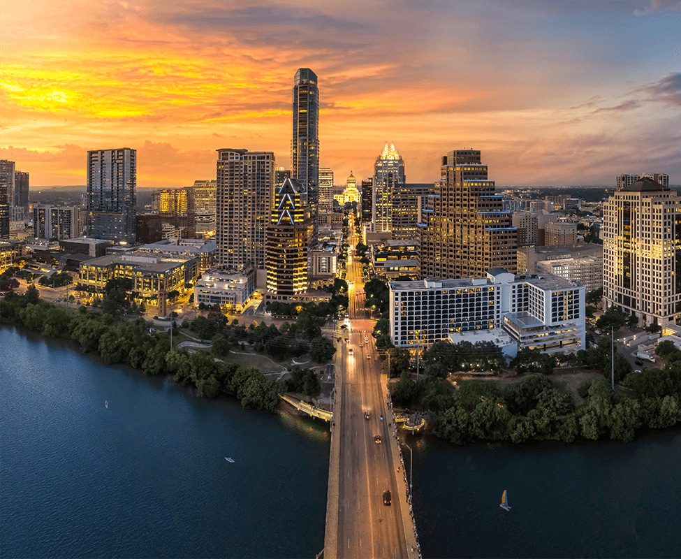 Austin skyline at sunset, featuring tall buildings along a river with a vibrant orange and purple sky.