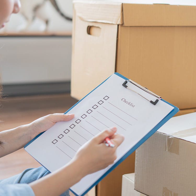 A woman with a clipboard sits on a chair, planning her relocation from Minneapolis, MN to Houston, TX.
