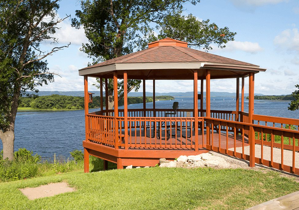 Onalaska: A wooden gazebo overlooks a calm lake, surrounded by green grass and trees under a blue sky with fluffy clouds.