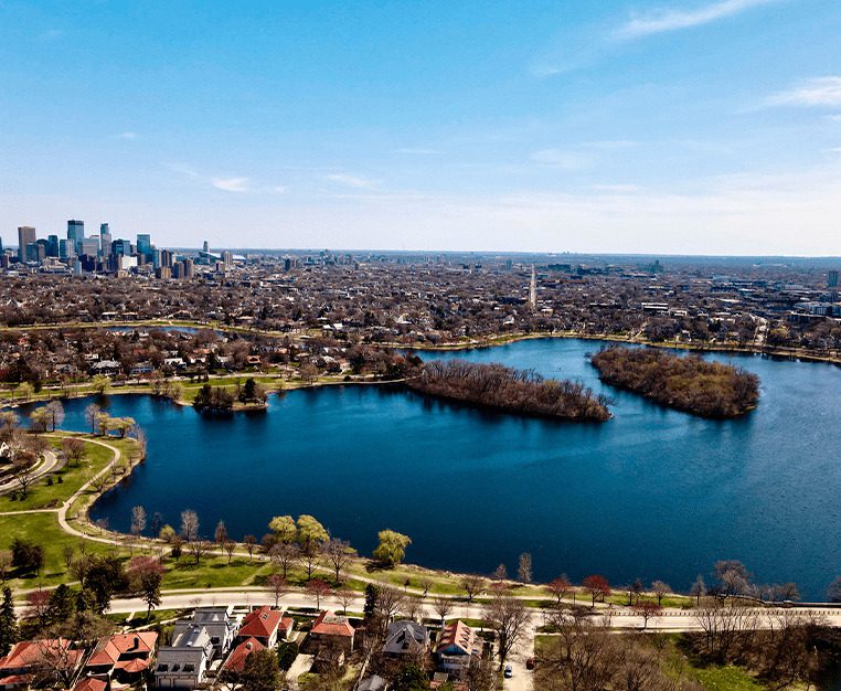 Aerial view of a city skyline beside a large lake with islands and green parks under a clear blue sky.