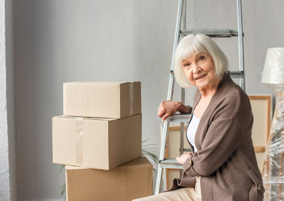 senior woman sitting on ladder with cardboard boxes on background, moving concept