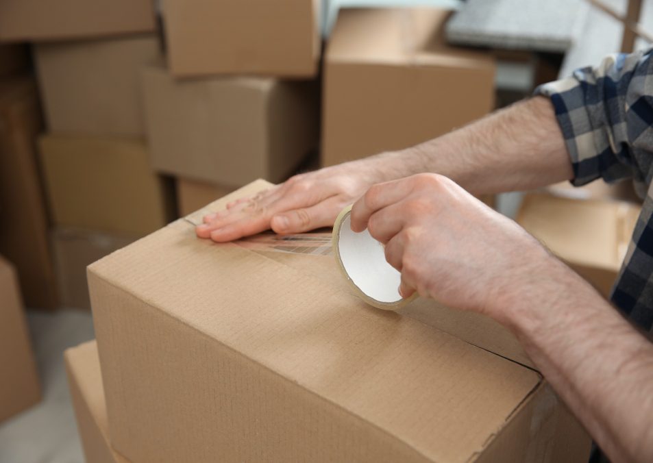 Man taping cardboard box indoors, closeup. Moving day